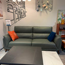 Green sectional sofa with colorful pillows in a living room setting.