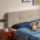 Modern beige upholstered bedframe with button detailing paired with blue bedding and a wooden bedside table